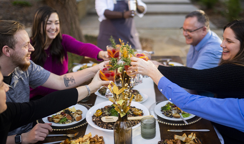 people sitting around table smiling and toasting drink glasses