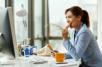 woman eating a granola bar while working at a computer